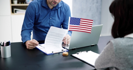 A man and woman review immigration application forms at a desk with a small United States flag. | The Law Offices of Eugene Mogilevsky, LLC